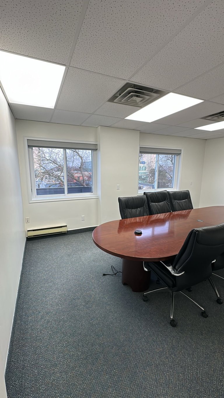 Modern office conference room with oval wooden table, black leather chairs, and windows overlooking bare trees
