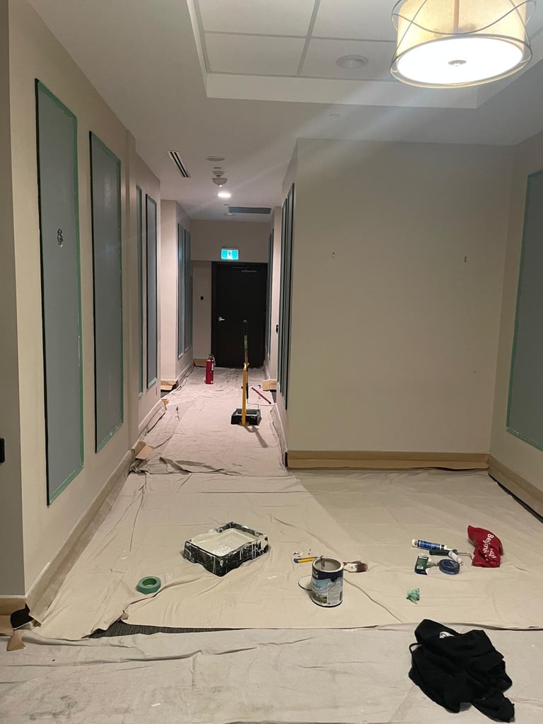 Interior hallway under construction with drop cloths, paint cans, and tools scattered on the floor during renovation