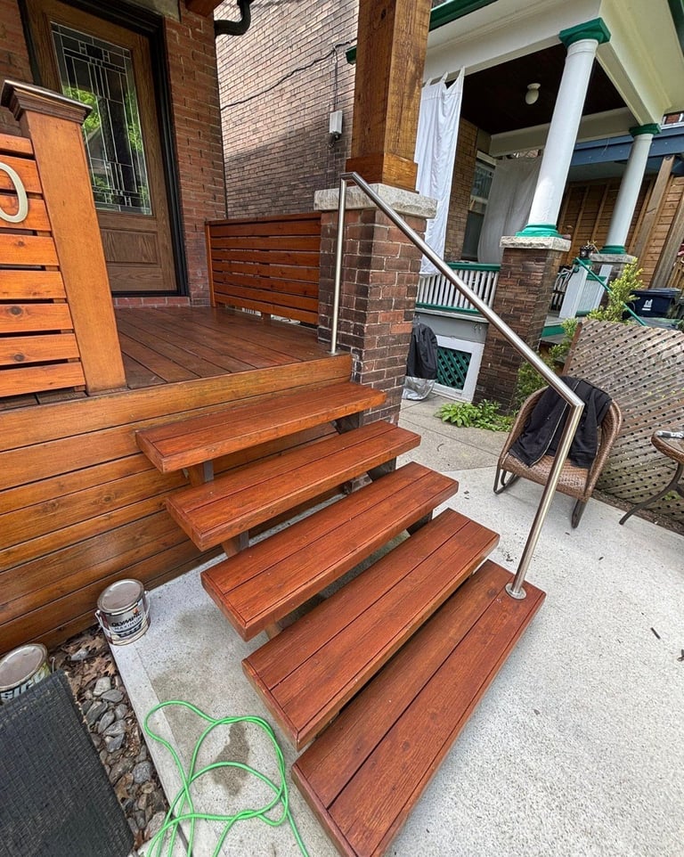 Wooden front porch steps with metal handrail leading to brick townhouse entrance, with a green garden hose coiled at the base