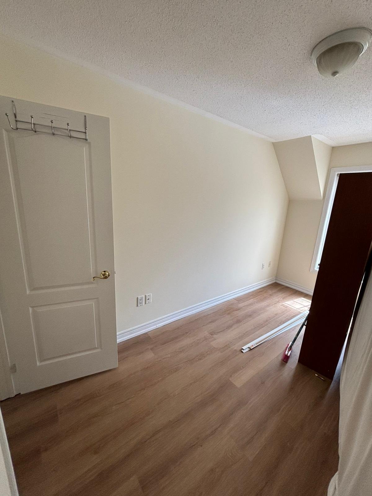 Empty bedroom with white walls, wooden flooring, two white doors, and a smoke detector on the ceiling
