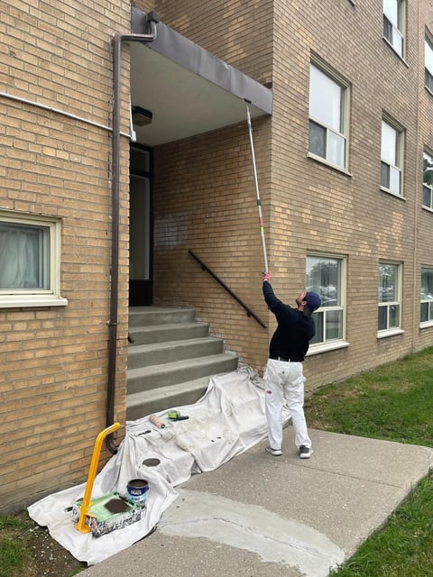Worker in white pants and black jacket pulling down a white awning or canopy attached to a brick building entrance