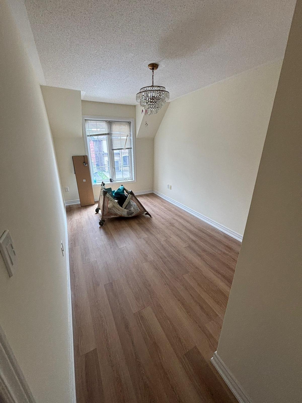 Empty room with cream walls, wooden flooring, chandelier, and a window with natural light