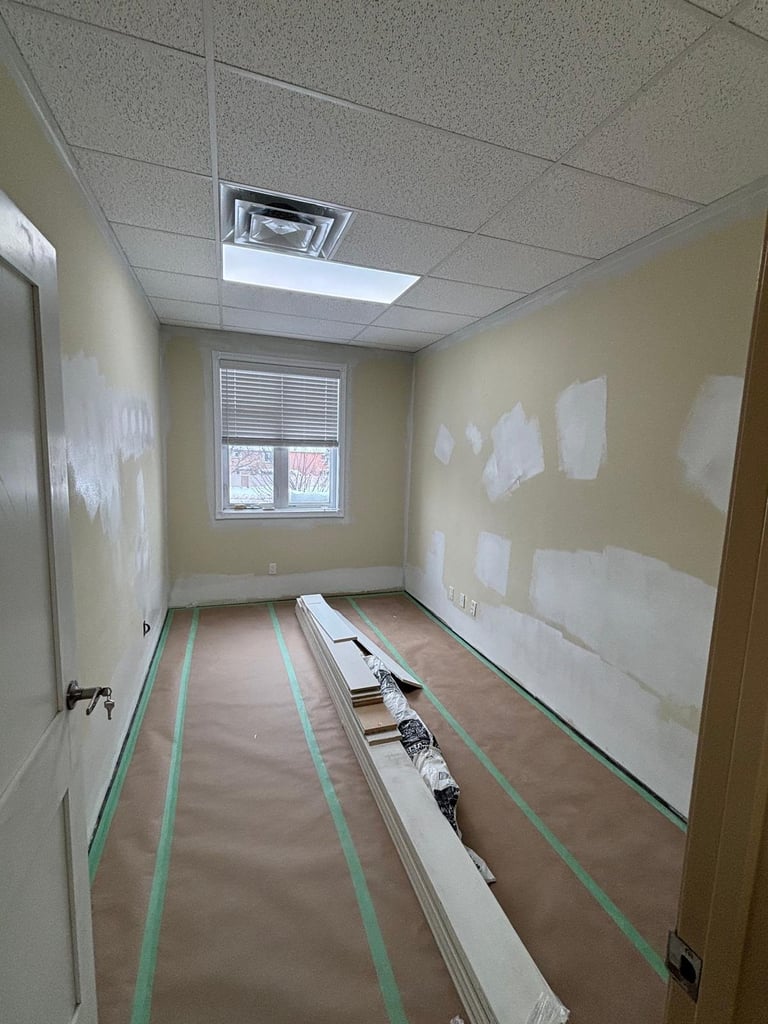 Interior room under renovation with taped walls, drop ceiling, window, and protective plastic sheeting on floor