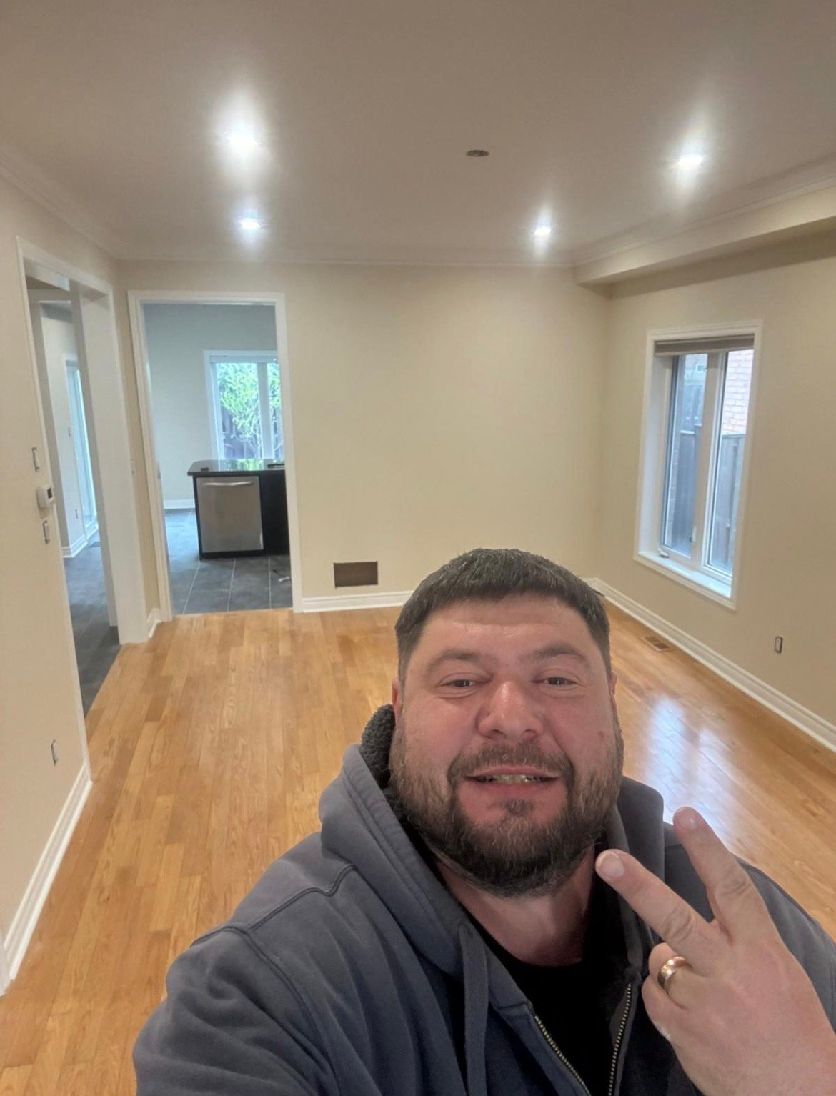 Man with beard in gray jacket taking selfie inside empty room with wood floors
