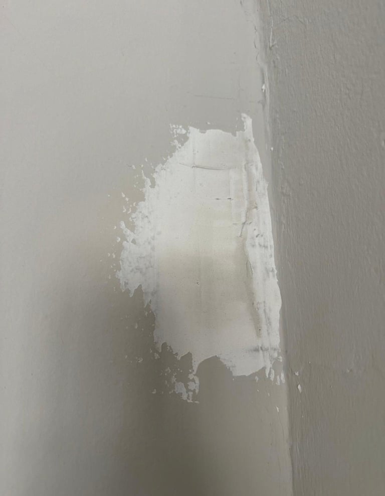 Drywall outlet box with white spackle and joint compound applied, showing patched wall repair work in progress