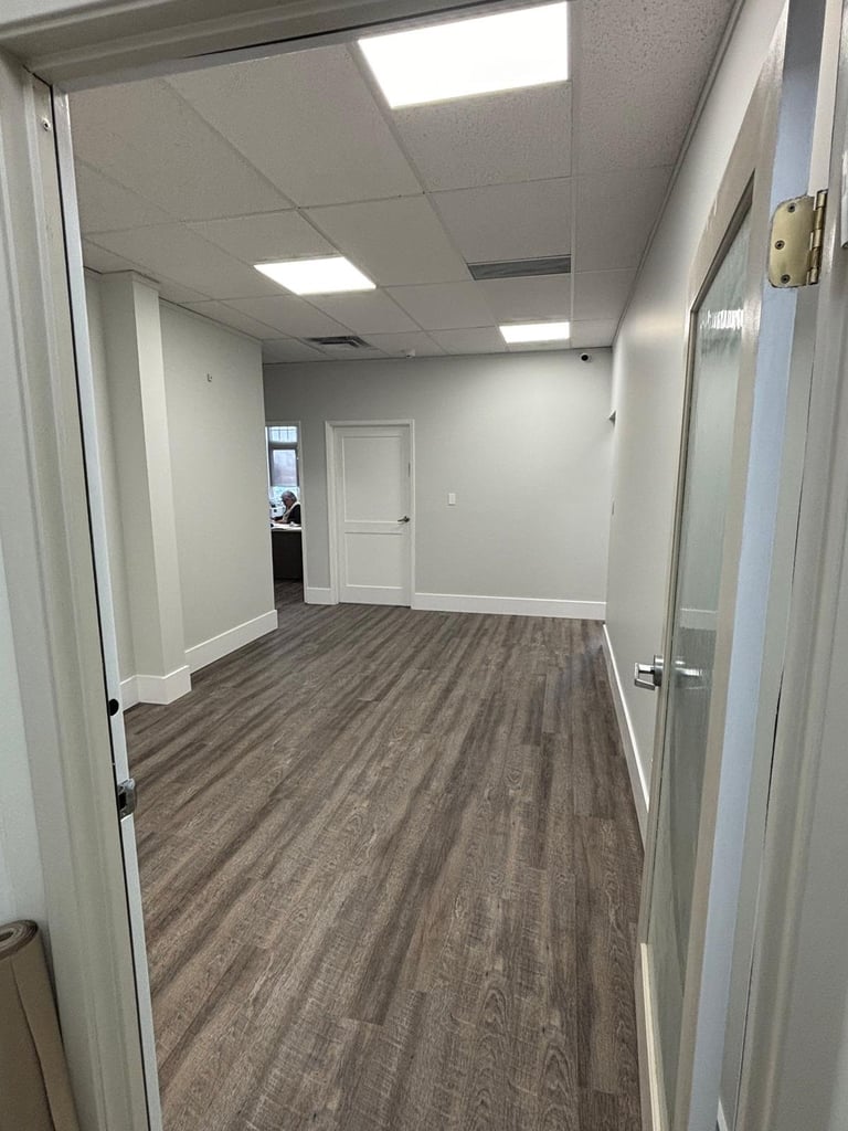 Empty office hallway with wood-look flooring, white walls, ceiling lights, and white doors on either side