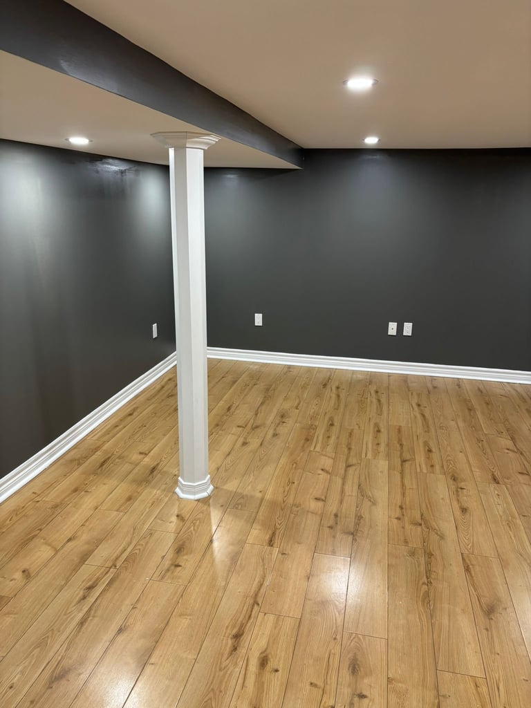 Modern basement room with dark gray walls, white trim, wooden floor, central support column, and recessed lighting