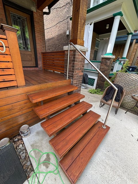 Red-brown wooden staircase with metal railing leading down to a brick townhouse entrance porch area