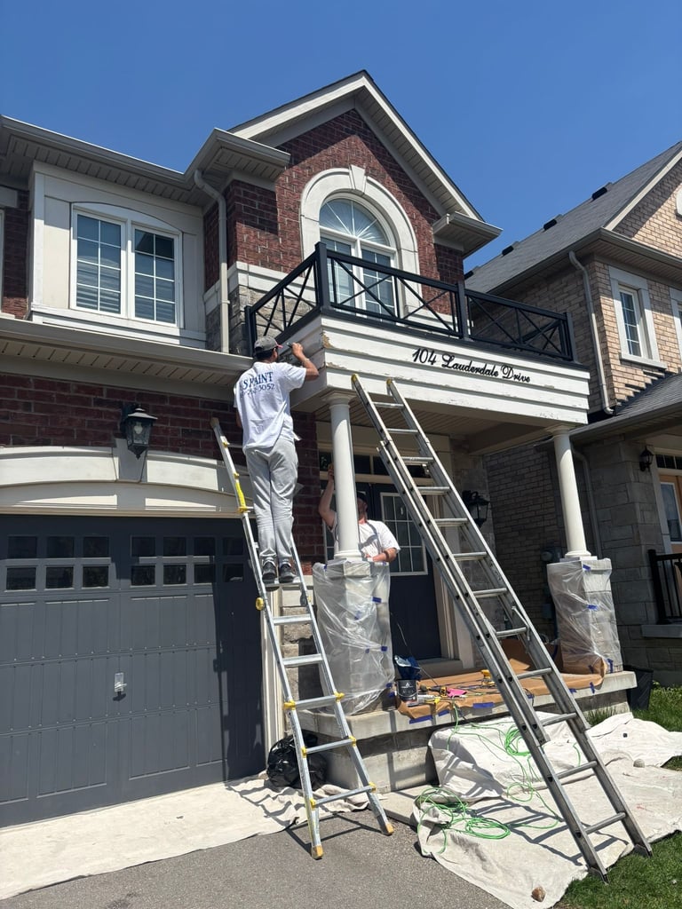 Painter on ladder working on exterior of brick residential home with garage