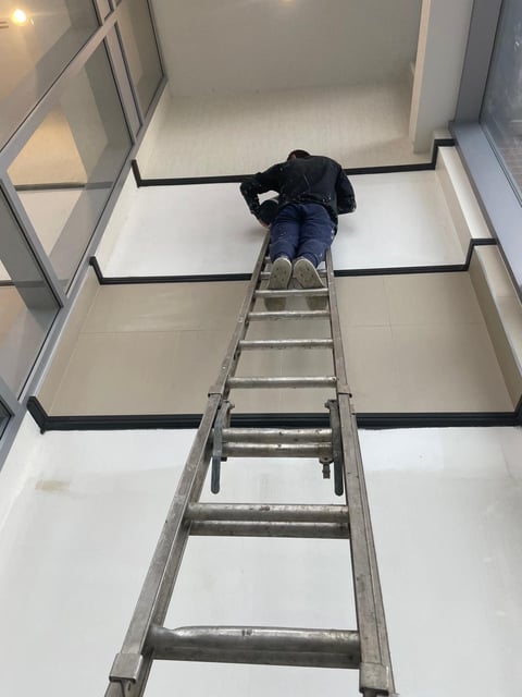 Person climbing a metal ladder up through an open ceiling or loft space indoors